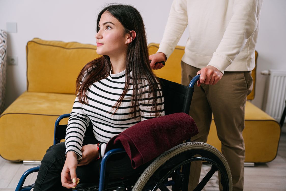 Caregiver assisting a person in a wheelchair at home, showing the warm and supportive attendant relationship